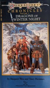 The cover of Dragons of Winter Night. Three figures stand in a snowy landscape. The first is a kender: short, ponytailed, and carrying a forked staff. The second is a blond-haired elven woman in armour, holding a long lance with a silver spearpoint. The third is a woman in scary-looking blue scale armour and a horned helmet standing in a power pose. Behind them, a blue dragon lurks in the snowy hills.